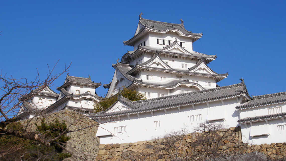 Close-up view of the main keep of a Japanese castle, showcasing its white plaster walls, tiled roofs, and stone base inside the paid area.