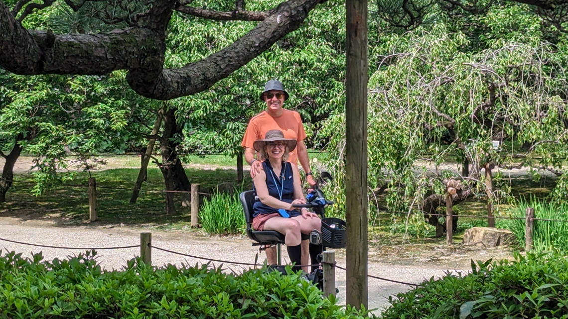 Anne de Ridder in her mobility scooter with her husband in a Japanese garden