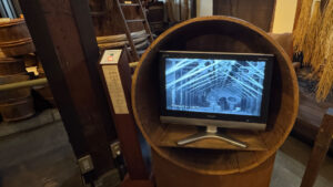 Video display in a wooden barrel showing a 1928 sake-making film. An English translation button is available for audio but not subtitles.