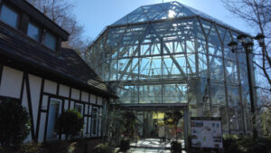 Glasshouse at Kobe Nunobiki Herb Gardens, featuring a geometric glass exterior with a nearby Tudor-style building.