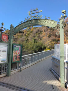 Entrance to Kobe Nunobiki Herb Gardens & Ropeway, featuring a decorative green archway and a tiled pathway by Shin-Kove Station.