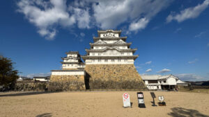 A view of the castle keep from Bizenmaru bailey, showcasing its towering white walls, stone base, and surrounding open courtyard.