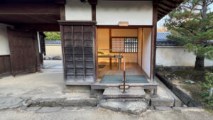 An entrance to an exhibition room with wooden flooring, accessed by three steps. A handrail is provided for support.