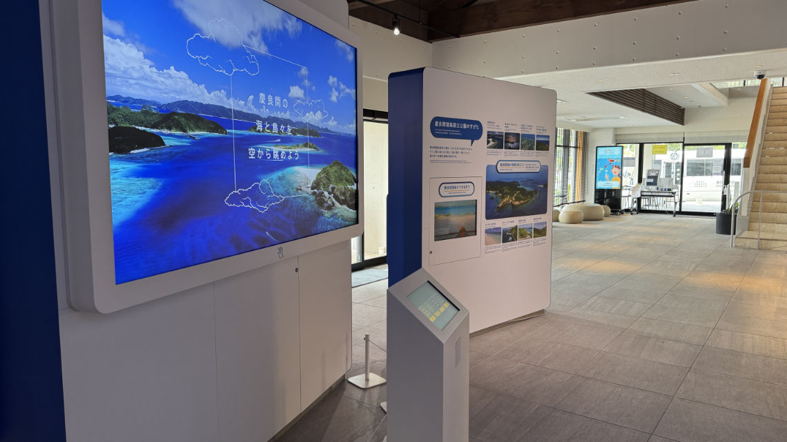 Modern visitor center interior with digital displays showcasing scenic views of islands and oceans, and an interactive information kiosk.