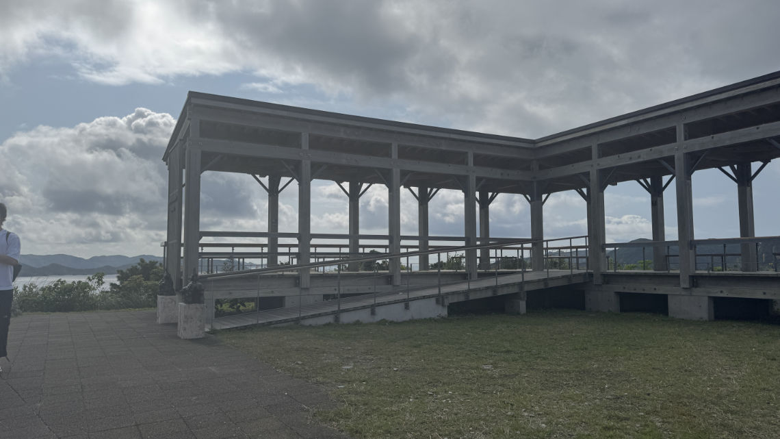 Wooden observation deck with ramps overlooking the sea and distant islands, under a partly cloudy sky.